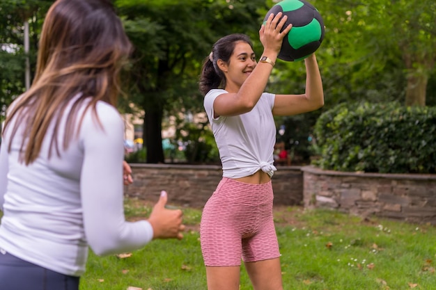 Latijns meisje dat sport doet in een groen park, een gezond leven leidt, attente leraar met de studenten in de oefening van squats met de gewichtsbal