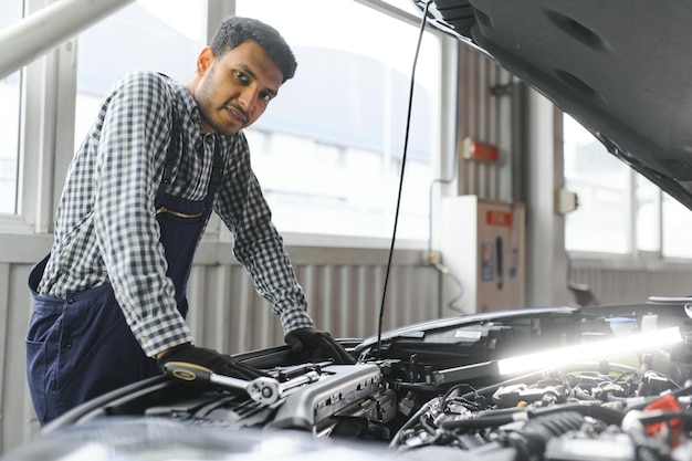 Latijns-Spaanse automonteur in uniform onderzoekt een auto terwijl hij in de autoservice werkt