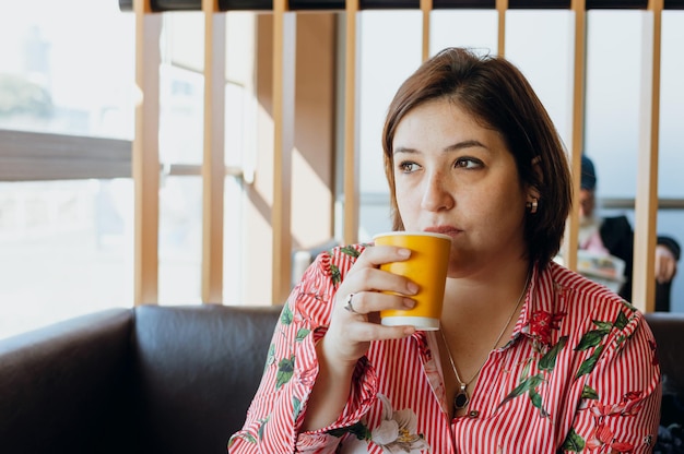 Latijnse jonge blanke vrouw die koffie drinkt en denkt zittend in een fastfoodrestaurant