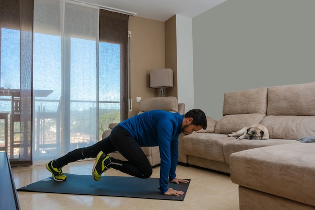 Latijnse man, aan het trainen in zijn woonkamer, doet sit-ups, rekoefeningen en squats