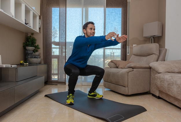 Latijnse man, aan het trainen in zijn woonkamer, doet sit-ups, rekoefeningen en squats