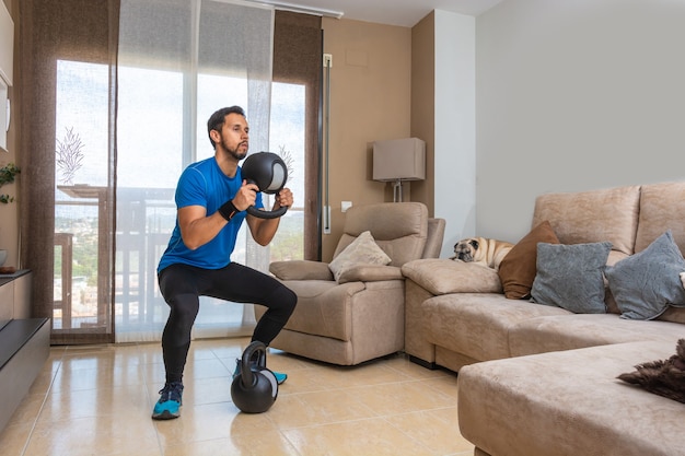 Latijnse man die thuis een cross-fit training uitvoert met een paar kettlebells.