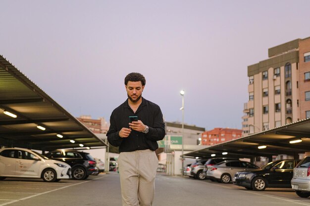 Latijnse man loopt met een mobiele telefoon op een parkeerplaats in de schemering