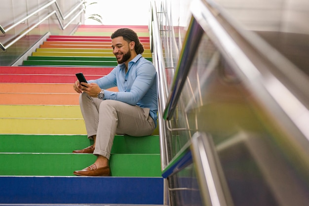 Latijnse man met dreadlocks zittend op een kleurrijke trap met zijn mobiele telefoon