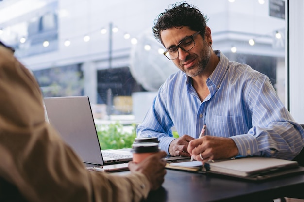 Latijnse man van middelbare leeftijd met een bril die aantekeningen maakt in een coffeeshop voor zijn laptop en zijn partner