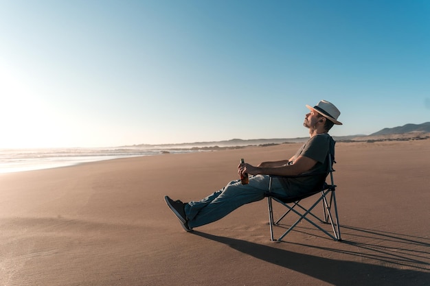 Latijnse man zit ontspannen aan de oever van het strand bier te drinken en naar muziek te luisteren