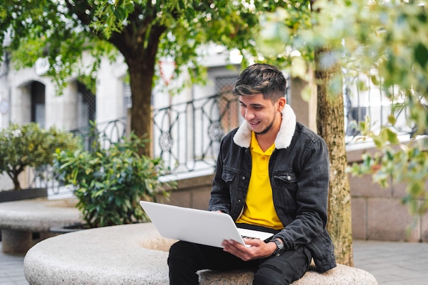 Latijnse man zit op een stenen bankje in het park met laptop