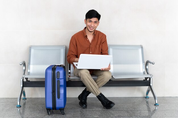 Latijnse man zit op station met koffer en werkt met laptop