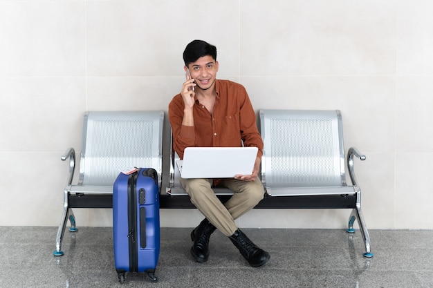 Latijnse man zit op station met koffer en werkt met laptop