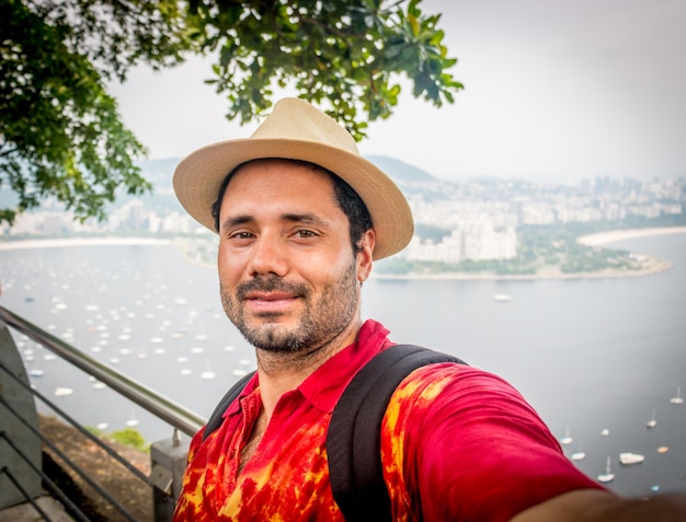 Latijnse toerist met hoed in Rio de Janeiro op Sugarloaf die selfies neemt en een gelukkig rood shirt glimlacht