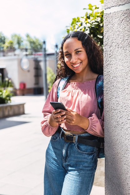 Latijnse universiteitsstudente vrouw die lacht en haar mobiel gebruikt om in haar vrije tijd buiten de campus te zitten