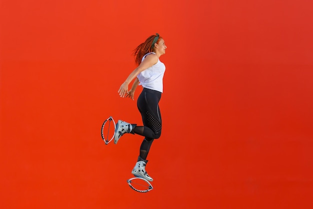 Latijnse vrouw die een oefeningsroutine doet met de Kangoo Jumps-laarzen op een oranje achtergrond. Gezond levensstijlconcept