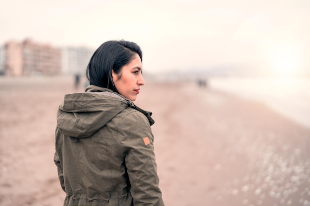 Latijnse vrouw die in profiel op het strand staat en naar de horizon boven de zee kijkt