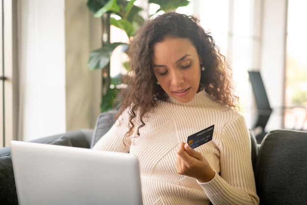 Latijnse vrouw die laptop en hand met creditcard gebruikt om thuis op de bank te winkelen