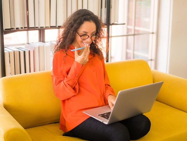 Latijnse vrouw die met laptop op bank thuis werkt