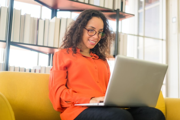 Latijnse vrouw die met laptop op bank thuis werkt