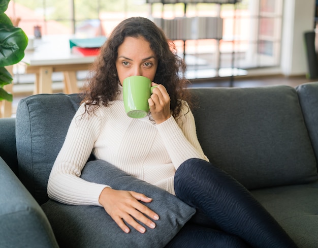 Latijnse vrouw die thuis koffie drinkt op de bank