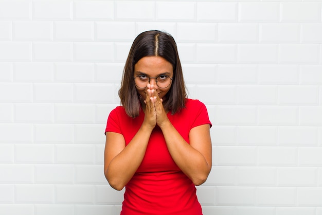 Latijnse vrouw die zich ongerust, hoopvol en religieus voelt, trouw bidt met de handpalmen ingedrukt en om vergeving smeekt