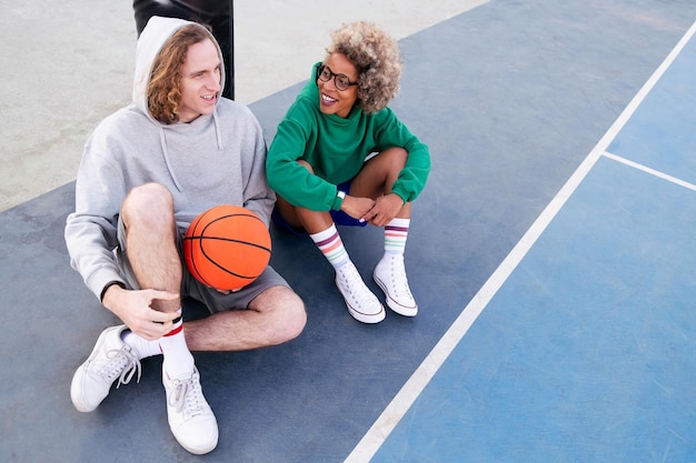 Latijnse vrouw en blanke man chatten gelukkig zittend op het basketbalveld na het spelconcept van vriendschap en stedelijke sport in de straat kopiëren ruimte voor tekst