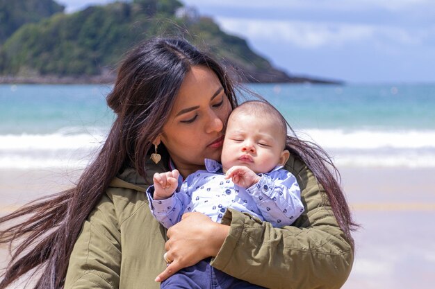 Foto latijnse vrouw kijkt teder naar het gezicht van haar baby op het strand en in de lente