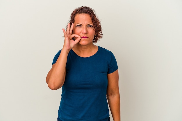 Latijnse vrouw van middelbare leeftijd geïsoleerd op een witte achtergrond met vingers op de lippen die een geheim houden.