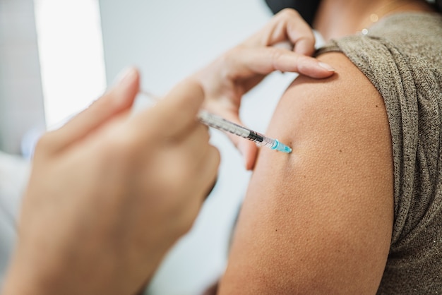 Latijnse vrouwelijke verpleegster die schot of vaccin geeft aan de schouder van een patiënt. Vaccinatie Covid 19 pandemie.