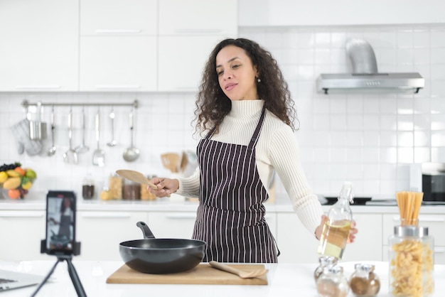 Latijnse vrouwen streamen online met een smartphone terwijl ze thuis in de keuken koken.