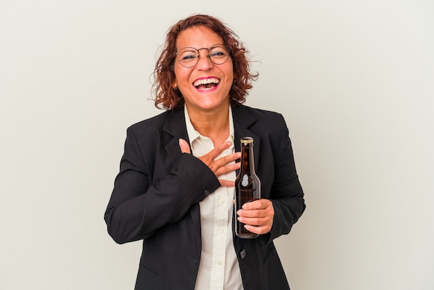 Latijnse zakenvrouw van middelbare leeftijd met een biertje op een witte achtergrond lacht hardop terwijl ze de hand op de borst houdt.