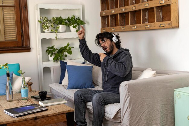 Latin American man sitting in his living room wearing headphones singing and enjoying his weekend