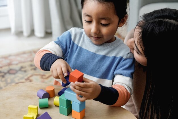 Latin american mother and son having fun playing with toy\
bricks at home family love concept