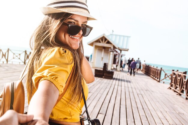 彼女のパートナーの手を前に歩いて保持しているラテンアメリカの旅行者の写真家の女の子