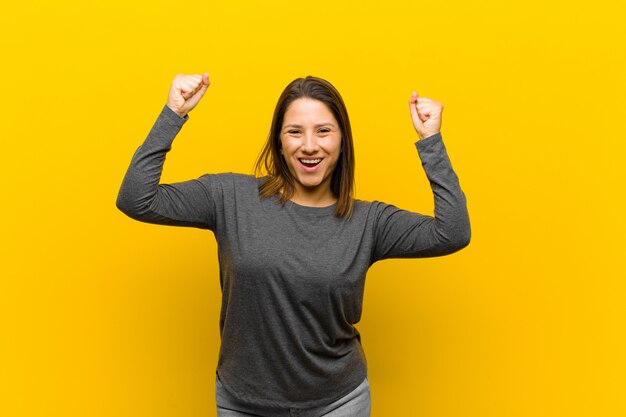 Latin american woman celebrating an unbelievable success like a winner, looking excited and happy saying take that! isolated over yellow wall