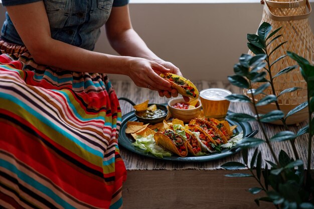 Latin american woman in traditional colorful skirt eating chicken tacos nachos salsa and guacamole