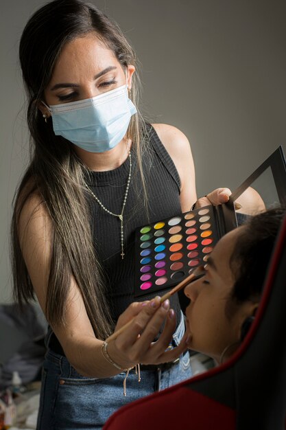 Latin American young woman putting makeup on a model with anti covid biosafety protocol