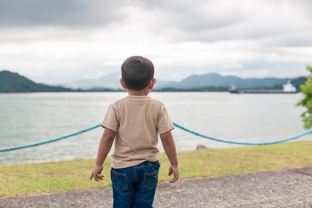 カーキ色のセーターを着て海に背を向けて立っているラテン系の少年