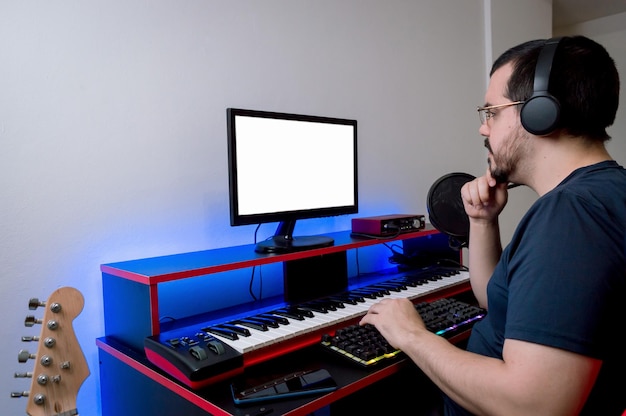 Latin caucasian man in his home music studio thinking with a hand on his chin watching the monitor