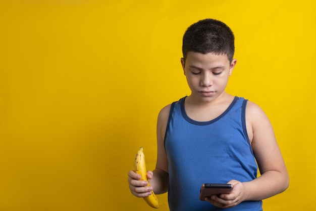 Latin child checking mobile with a banana in hand, on yellow background