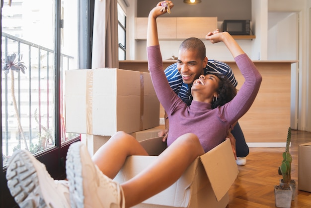 Latin couple having fun with cardboard boxes in new house.