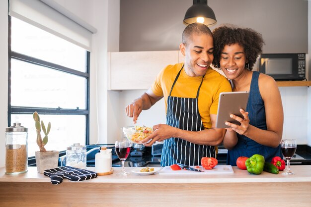 Latin couple using a digital tablet while cooking in kitchen.