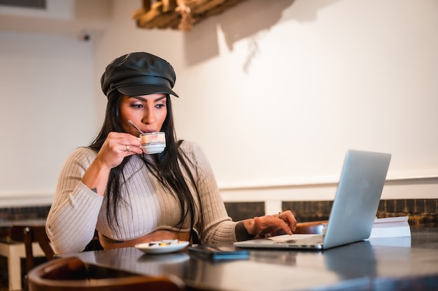 Latin fashion designer making some designs in a cafeteria with her laptop, having a coffee