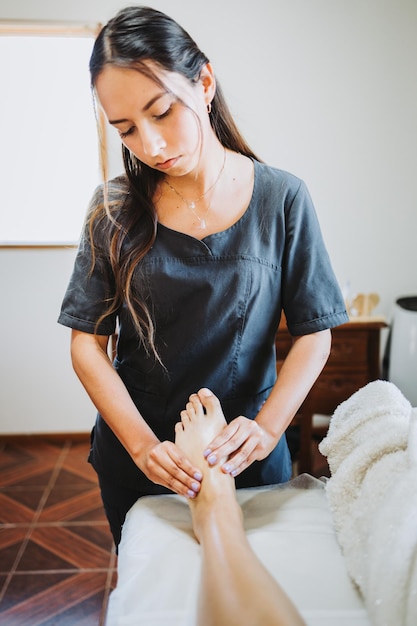 여성 환자에게 발 마사지를 하는 라틴 여성 치료사 웰빙 센터 스파 발 관리