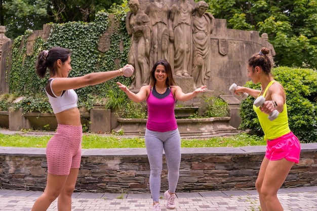 都会のライフスタイルの公園でスポーツをしているラテンの女の子、ウェイトを使って運動をしている生徒に指示を与える健康的な生活の先生