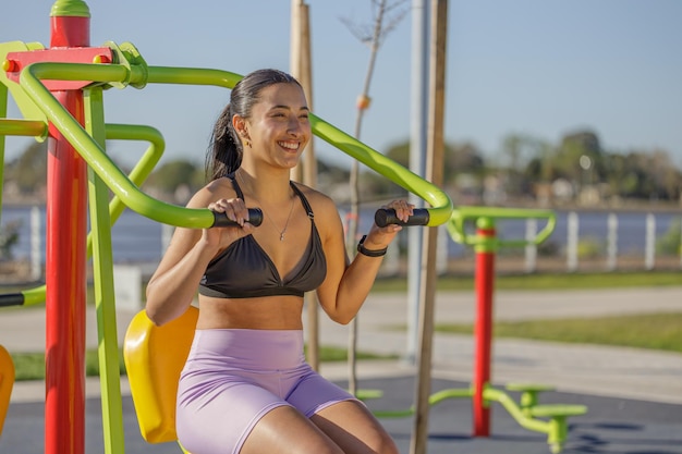 라틴계 소녀 가 공원 에서 운동 기계 에서 팔 을 운동 하고 있다
