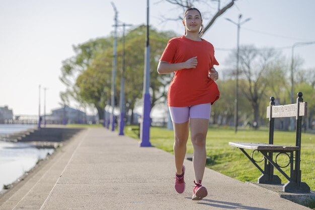 Latin girl in red tshirt running along the river boardwalk at dawn