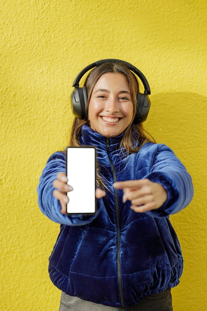 ヘッドフォンをかけたラテン系の女の子が携帯電話の空白画面を表示する
