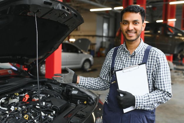 Latin hispanic auto mechanic in uniform is examining a car while working in auto service