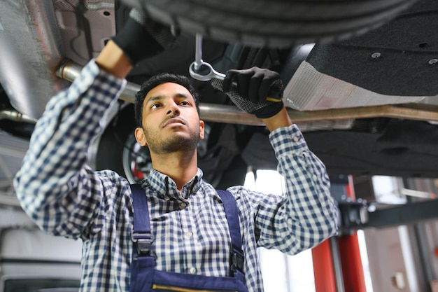 Latin hispanic auto mechanic in uniform is examining a car while working in auto service