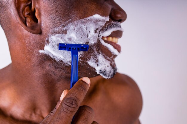 Latin hispanic man with razor and shaving foam on his face studio white isolate background