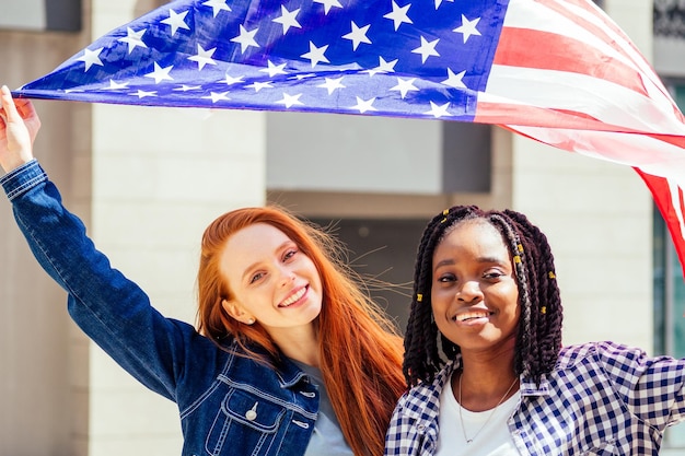 通りで米国旗を保持しているラテンヒスパニックと赤毛の生姜の女性