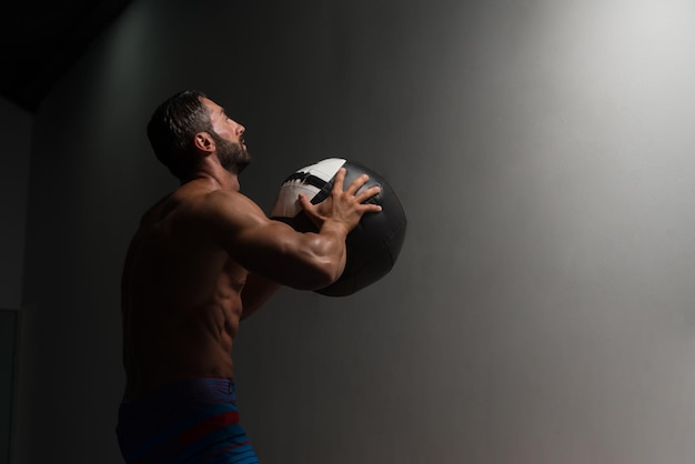 Foto atleta maschio latino accovacciato facendo esercizi di palle da parete in palestra